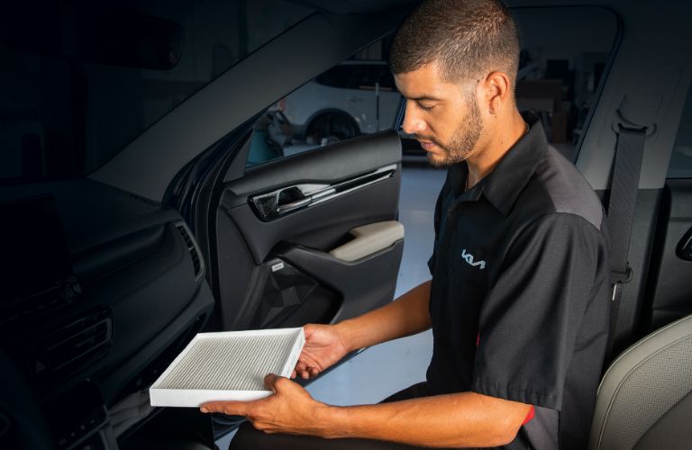 Kia technician holding a cabin air filter inside car